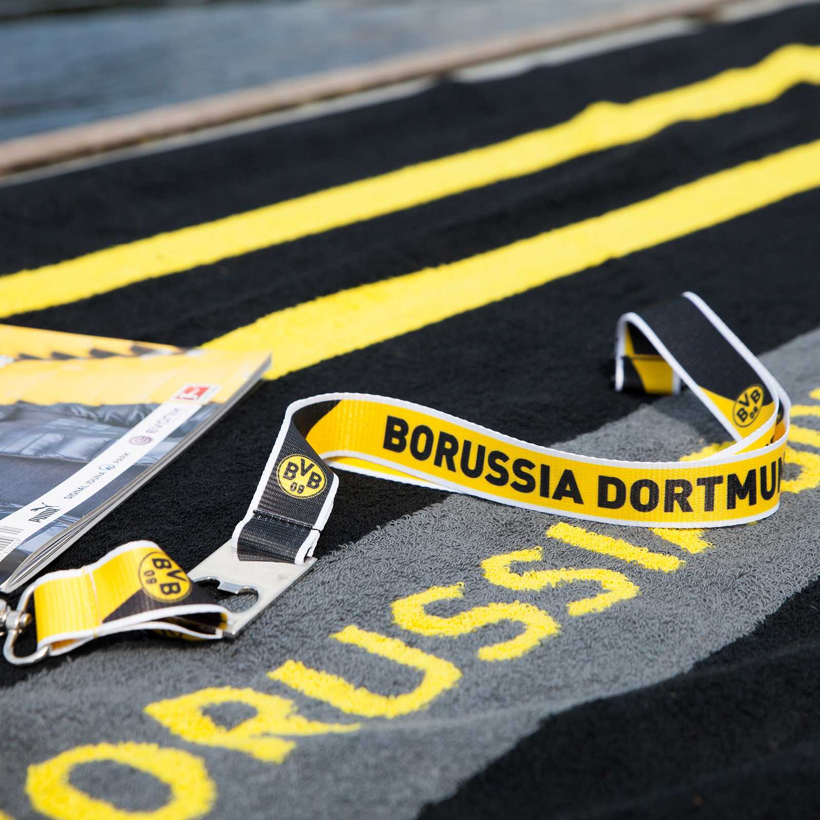 Detailansicht des BVB-Schlüsselbands mit Flaschenöffner in schwarzgelb, BVB-Emblem und "BORUSSIA DORTMUND"-Schriftzug sind sichtbar.