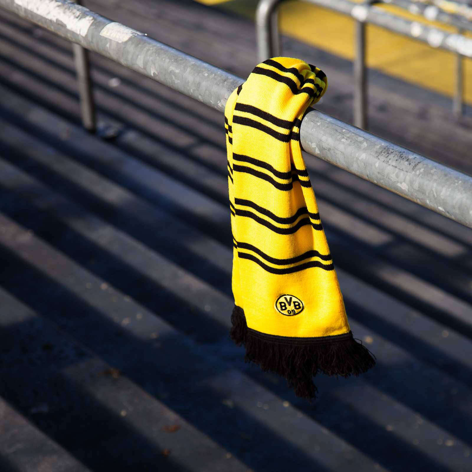 Detailansicht des BVB-Schals mit Ringelstreifen in gelb und schwarz, mit BVB-Emblem und schwarzen Fransen, hängend an einer Tribünenstange.