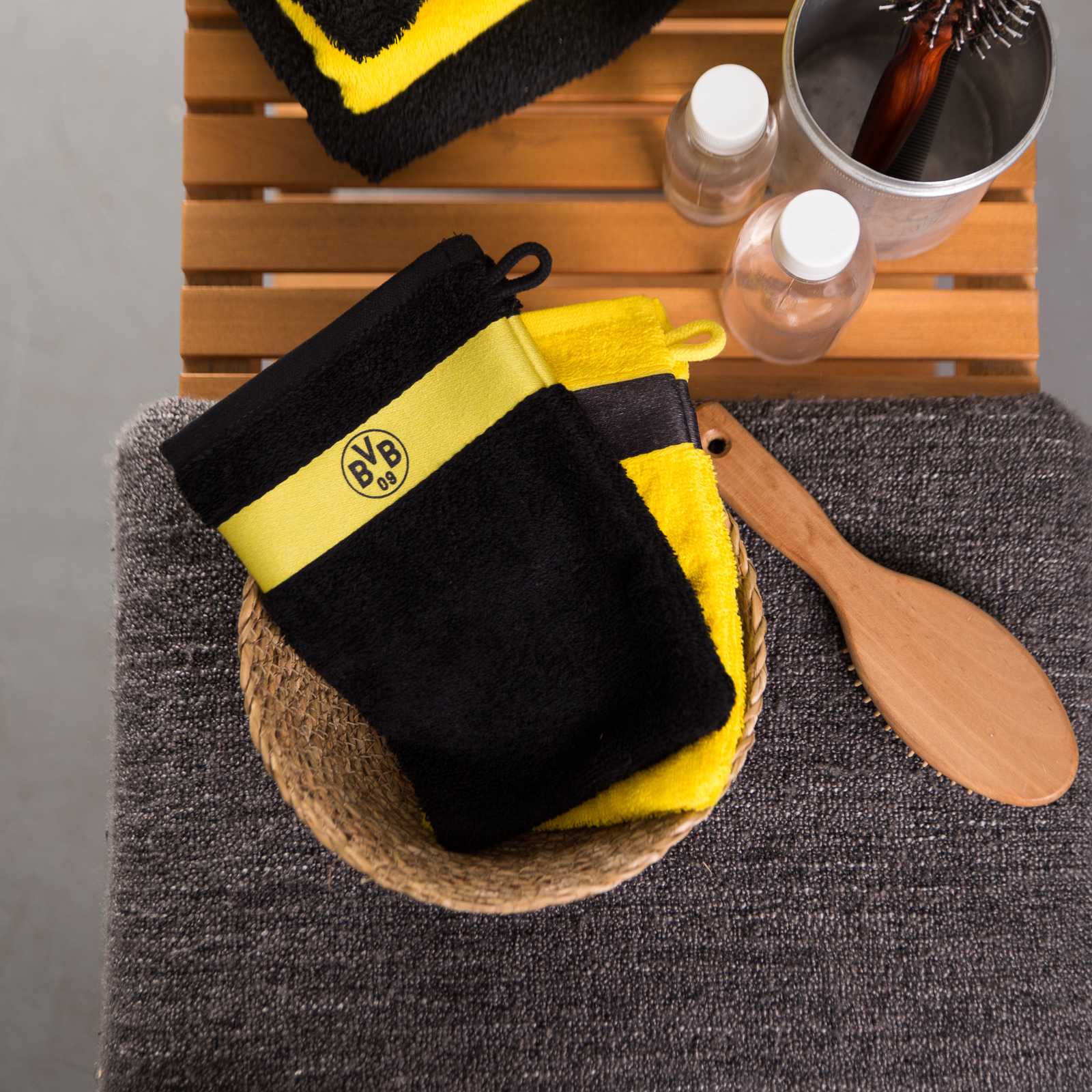 Frontalansicht des BVB-Waschhandschuhs (schwarz) mit gelbem Streifen und BVB-Emblem, liegend auf einem grauen Handtuch in einem Badezimmer-Setting.