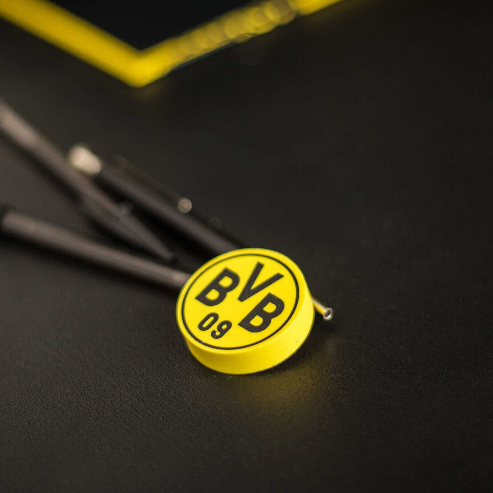 Detailansicht des runden BVB-Radiergummis in schwarzgelb mit großem BVB-Emblem auf der Vorderseite, auf dunklem Hintergrund liegend.