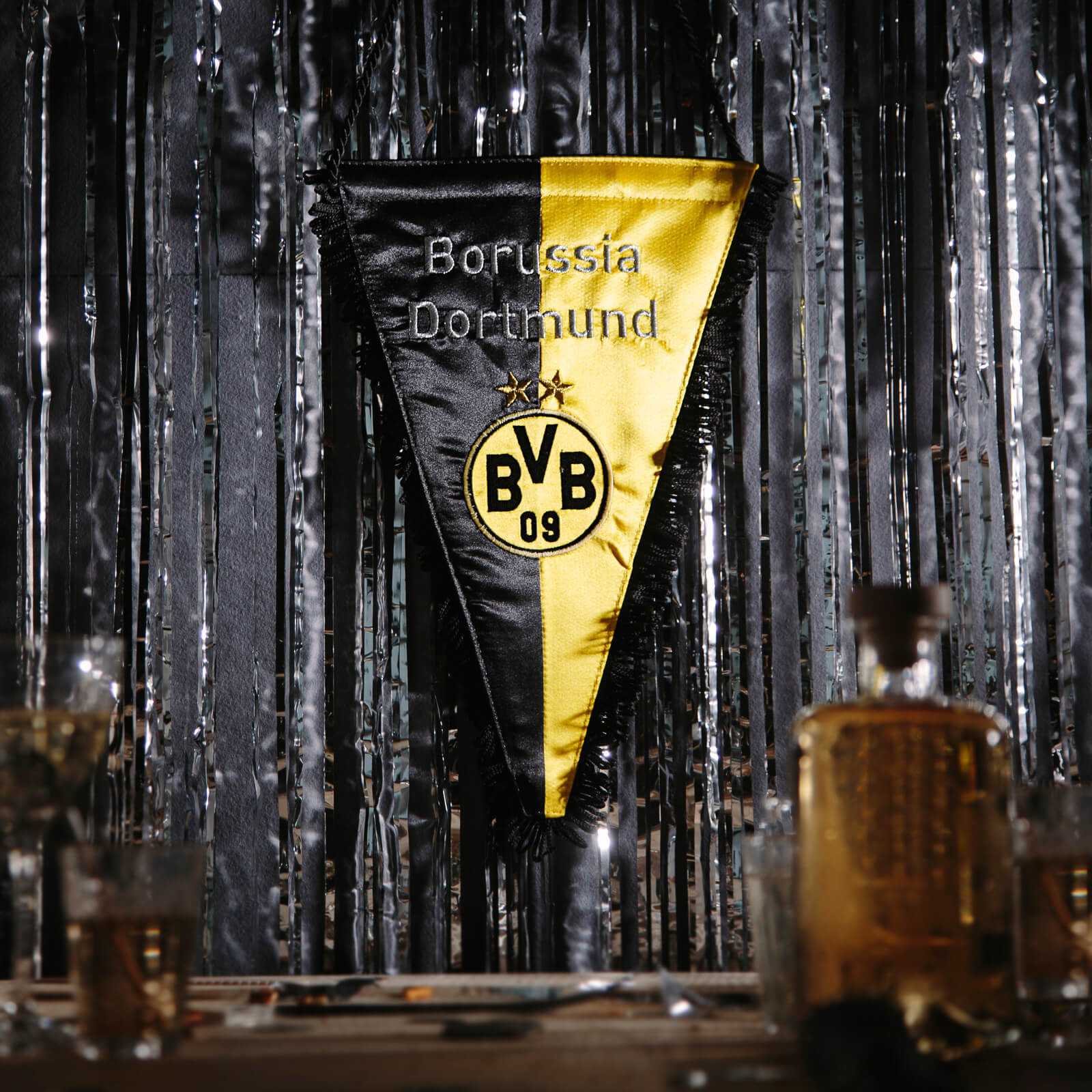 Vorderansicht des schwarzgelben BVB-Seidenwimpels mit BVB-Emblem und silberner Aufschrift "Borussia Dortmund" vor glitzerndem Hintergrund.