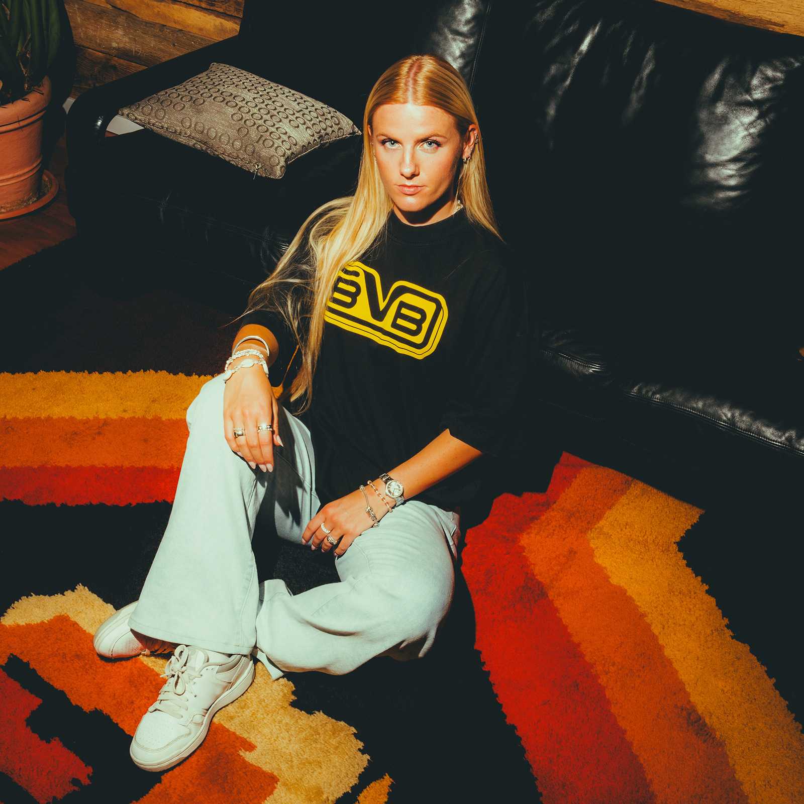 Eine Frau trägt das BVB Retro T-Shirt schwarz mit großem gelbem BVB-Schriftzug auf der Vorderseite, Sitzansicht in Wohnzimmer-Atmosphäre.