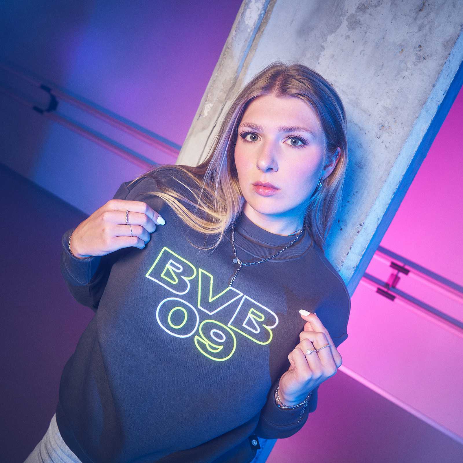 Frau trägt den BVB Neon Crewneck Damen in dunklem Grau, mit großem neongelbem „BVB 09“-Schriftzug auf der Vorderseite, Frontalansicht.