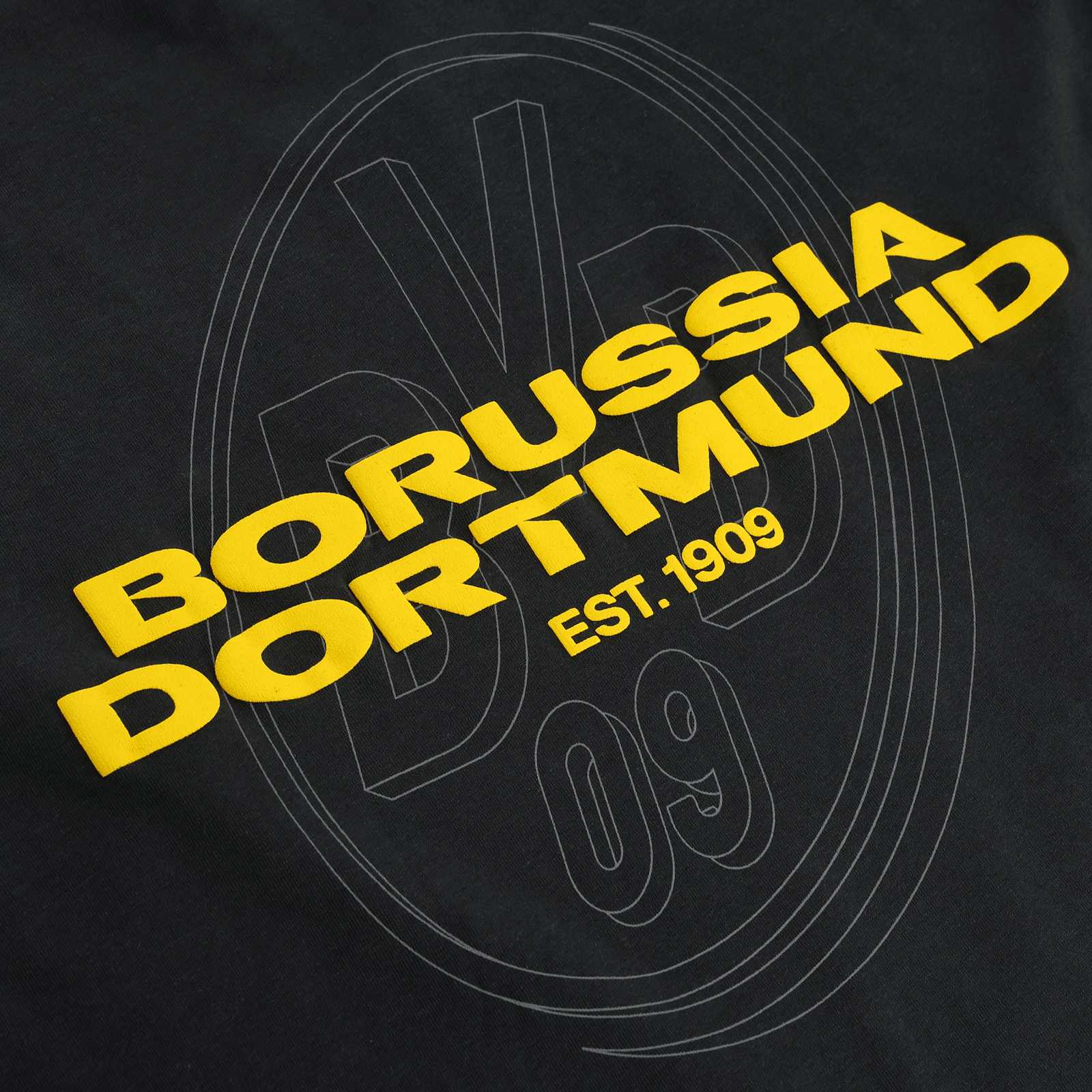 Detailansicht des BVB Urban Tee anthrazit 2025 mit großem gelben Schriftzug "Borussia Dortmund" und dezenter BVB 09-Logografik im Hintergrund.