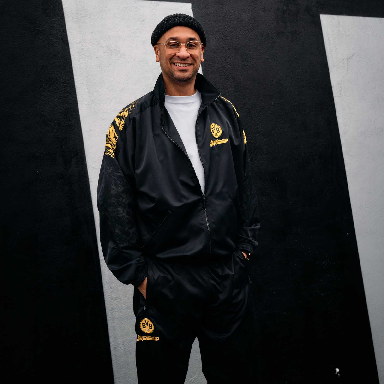 Jean Pierre trägt im schwarzen Trainingsanzug mit BVB-Logo und JP Performance Branding.