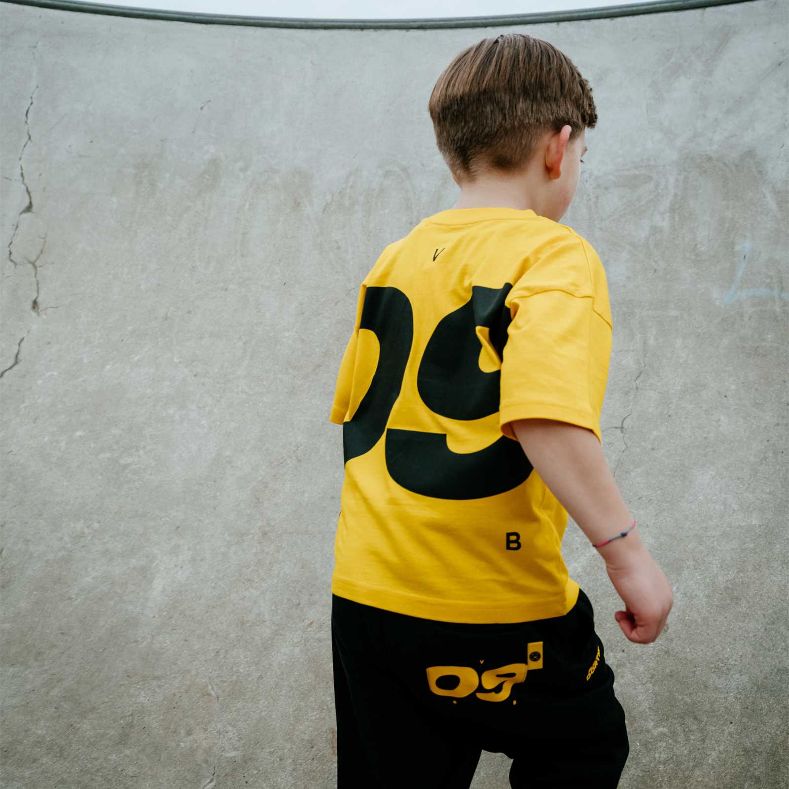 Kleiner junge läuft vor der Kamera weg und ist von hinten fotografiert. Er trägt ein gelbes BVB-Shirt und eine schwarze BVB-Hose, beide mit 09-Aufschrift auf der Rückseite.