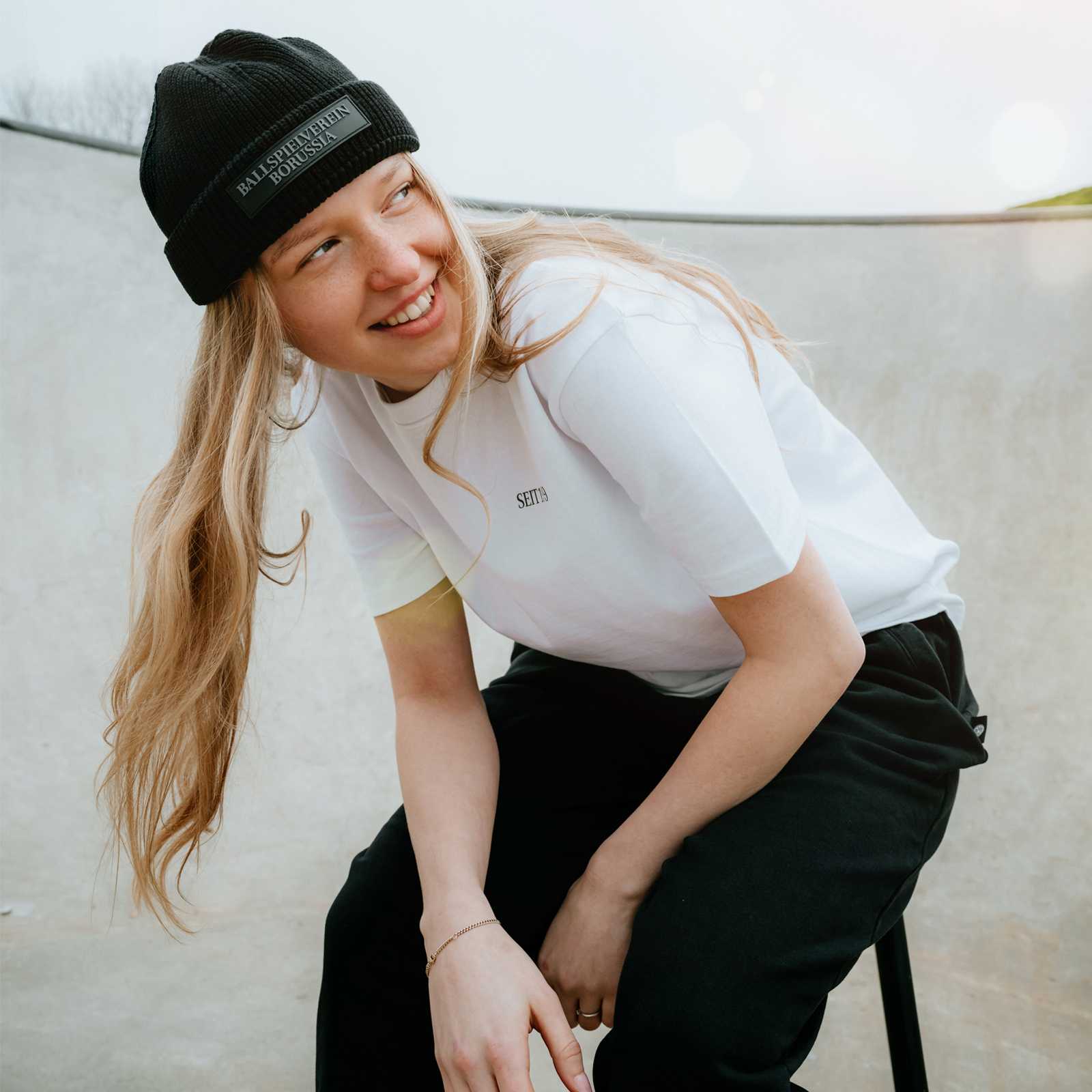 Ein weibliches blondes Model mit weißem T-Shirt trägt die schwarze Mütze