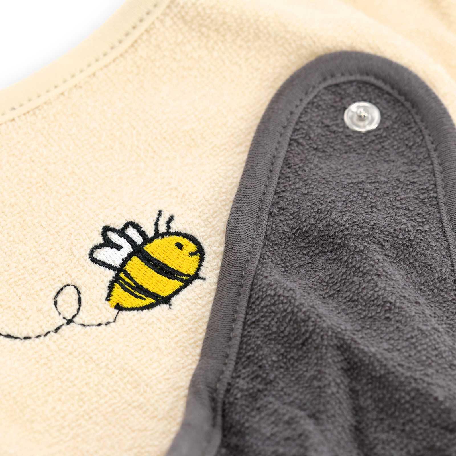 Detailansicht der kleinen Bienen auf dem beigen Tuch sowie der Knopf des grauen Tuches.