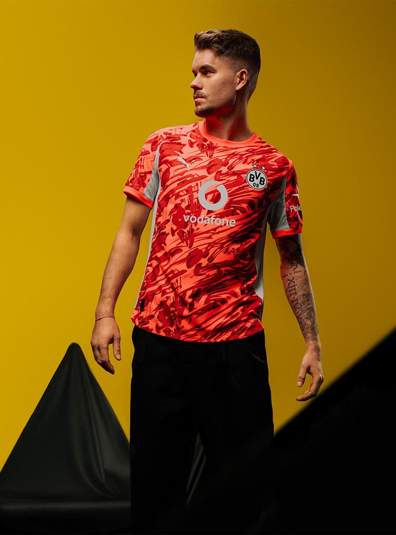 BVB-Torwart Meyer vor gelbem Hintergrund in dem neuen roten BVB-Heimtrikot 25/26.