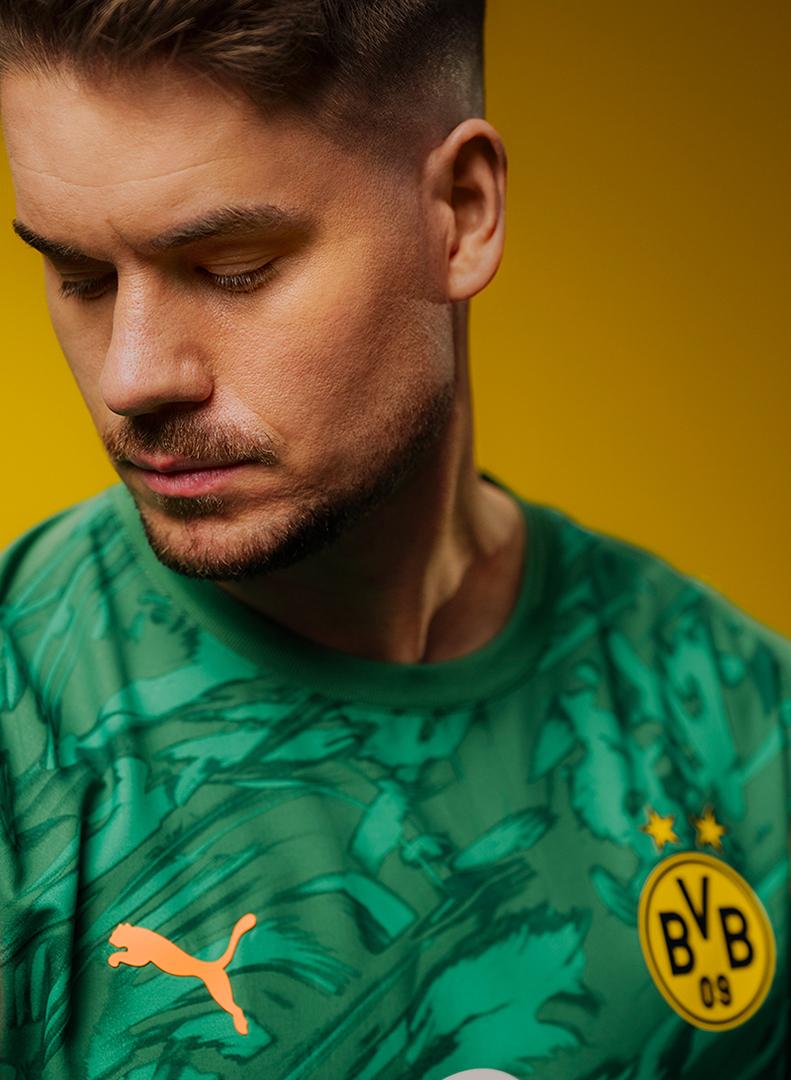 BVB-Torwart Meyer vor gelbem Hintergrund in dem neuen grünen BVB-Heimtrikot 25/26.